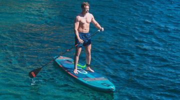 Person paddleboarding on calm and crystal-clear waters.